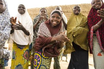 A girl clapping and smiling in niger, surrounded by other girls and women