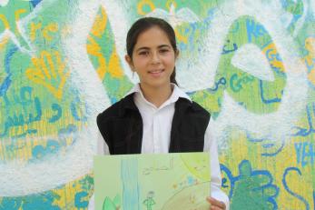 Nagham holding a piece of artwork in front of a brightly-painted wall