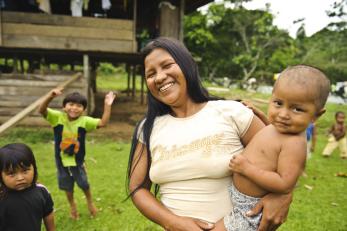 A smiling mother holds an infant in colombia with other children playing nearby