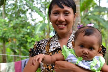 A woman holds a baby outside with trees in background in indonesia