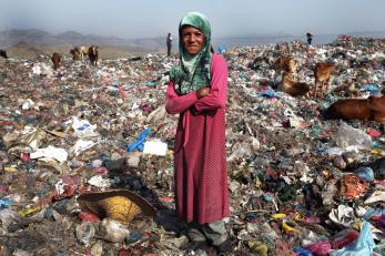 A woman in yemen standing among trash with cows in the background