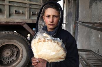 A boy wearing a black hooded sweatshirt holds bread in Syria