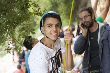 Young man in white t-shirt holding a yellow climbing rope and wearing a blue helmet