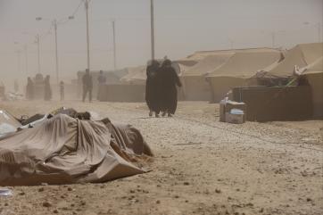 Woman navigate the dusty streets of a refugee camp.