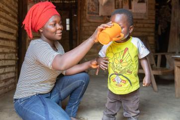 A farmer drinks water from a nearby mercy corps water tap with their 5 year-old son.