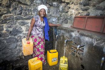 Noella pictured filling water containers at a row of taps