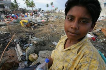 Boy in yellow shirt in front of rubble and debris