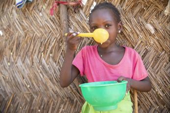 Girl in niger holding a large green bowl and yellow spoon
