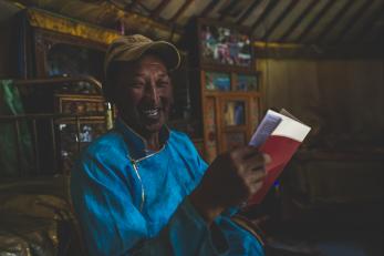 Batsaikhan sitting inside a yurt, holding a book and smiling