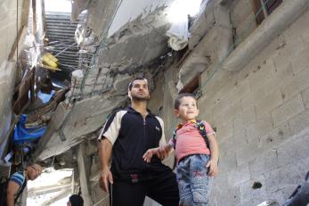 A man holds his son's hand as they survey the damage in their partially destroyed home in gaza