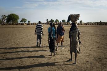 A group of people in south sudan walking across a dry landscape, pictured from behind