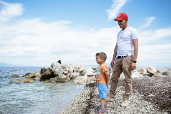 Ahmed, 3, with mercy corps staff member at a rocky beach in greece