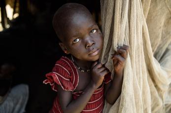 Young south sudanese girl clutching cloth door of tent.