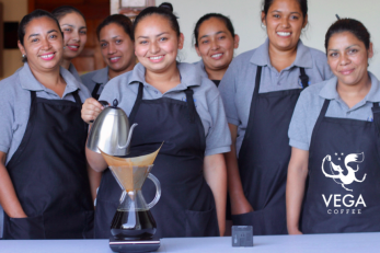 Seven women standing together, wearing dark blue aprons and brewing coffee