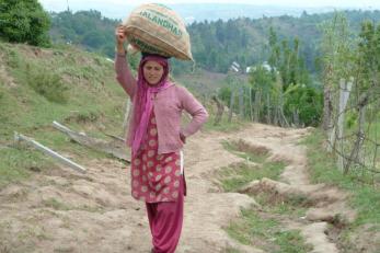 Farmer carrying bag of potato seed on her head, supported by her hand