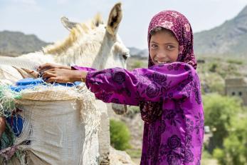 Girl in Yemen next to animal carrying water