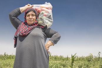 A woman in Syria carries a plastic bag filled with vegetables on her shoulder