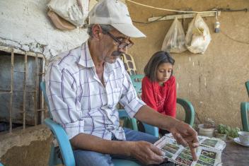 Abu Goubran looks through a seed catalogue with his daughter Dou’aa, 10, outside their house. Because this village is farther away from active fighting, Mercy Corps is able to work with the community to promote greater access to more diverse foods. Altogether, this farm directly supports four families.